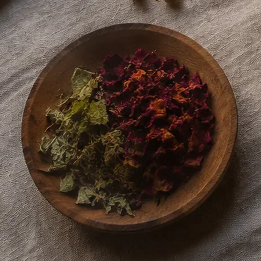Wooden bowl of dried rose petals and tea leaves resting on a linen cloth